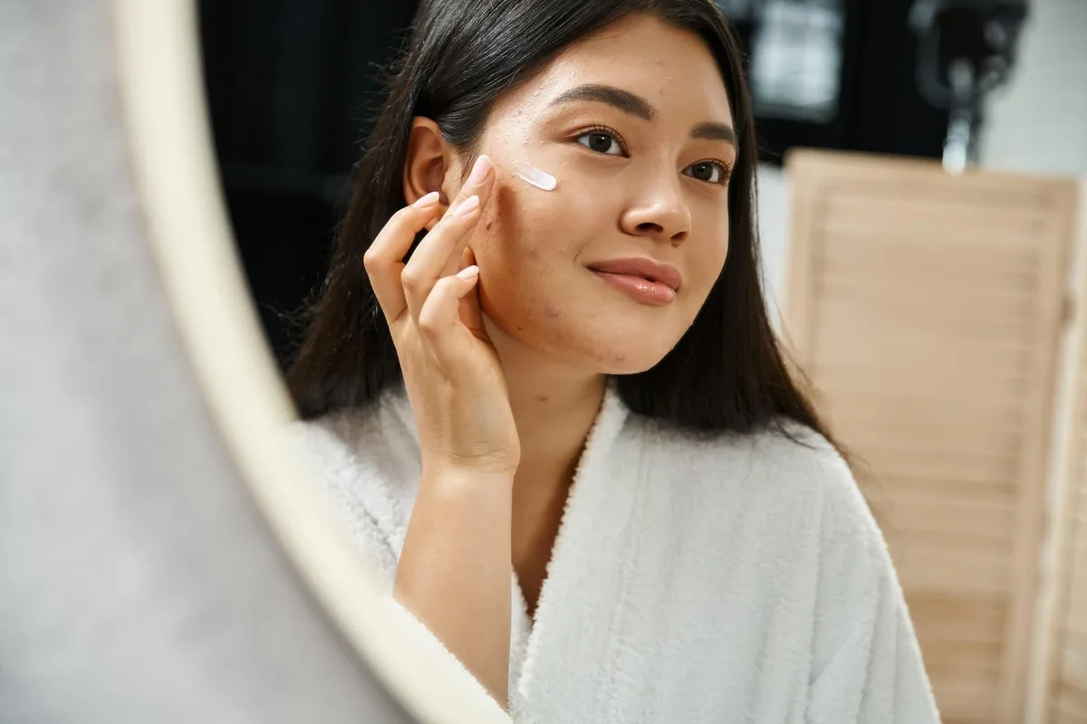 A woman applying moisturizer in the mirror as part of her daily pre-wedding skincare routine, which starts months before the wedding.