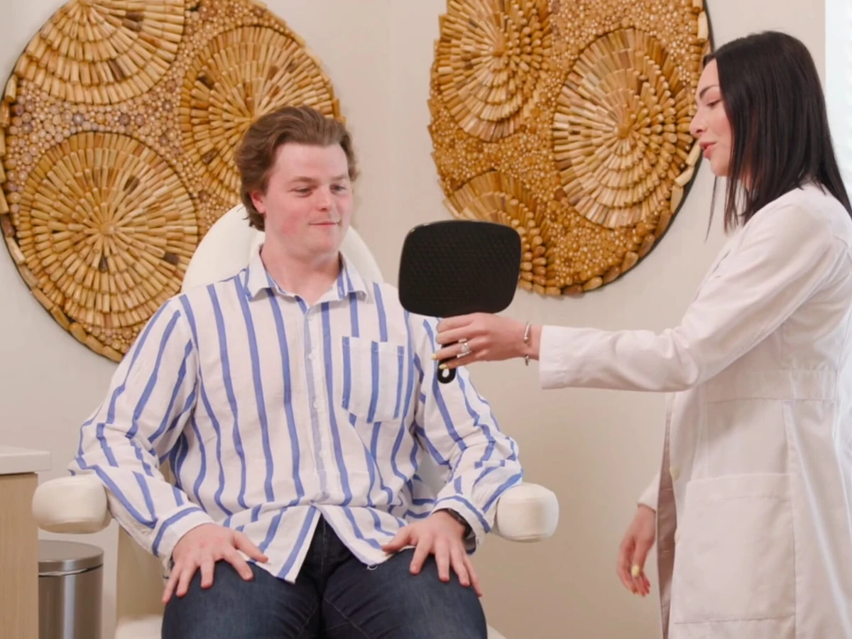 A male patient checking his skin in a hand mirror with Dr. Olivia after a men's facial consultation at Coastal Health & Medical Spa in Jacksonville, FL